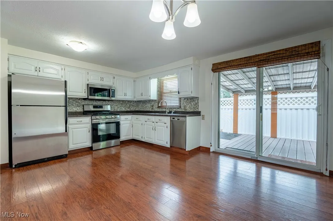 Kitchen with appliances with stainless steel finishes, dark countertops, backsplash, and white cabinetry