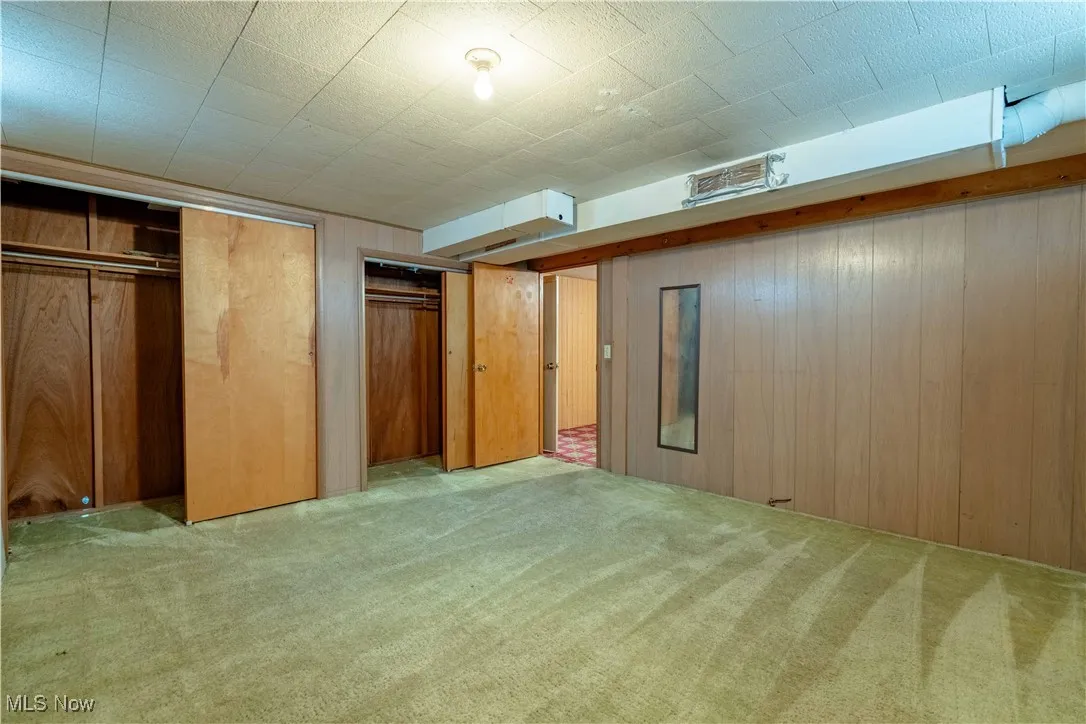 Unfurnished bedroom featuring light carpet and wood walls