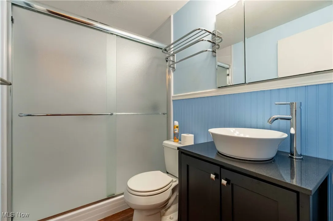 Full bathroom with a shower stall, vanity, wainscoting, and wood finished floors