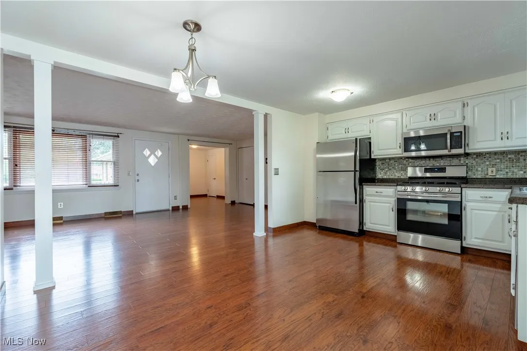 Kitchen with stainless steel appliances, hanging light fixtures, white cabinets, decorative backsplash, and dark wood-type flooring