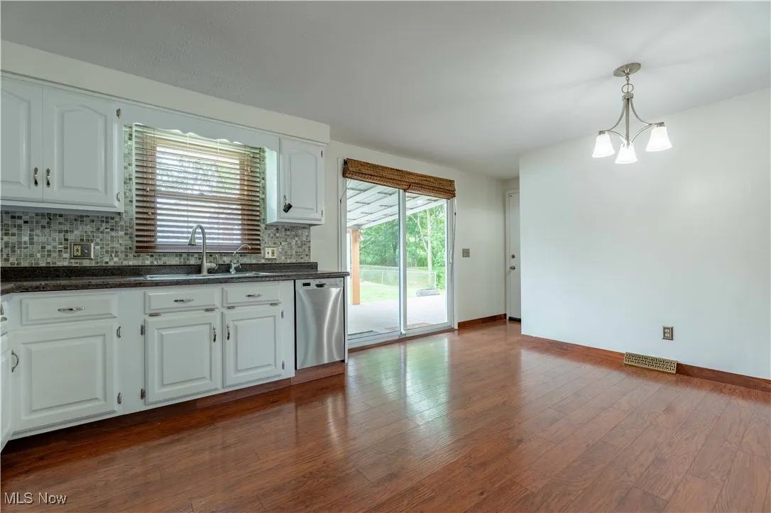 Kitchen with white cabinets, backsplash, dark stone countertops, dark wood-style flooring, and dishwasher