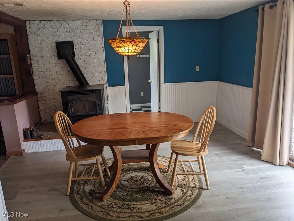 Dining area with a wood stove, a textured ceiling, vinyl plank floors, and wainscoting
