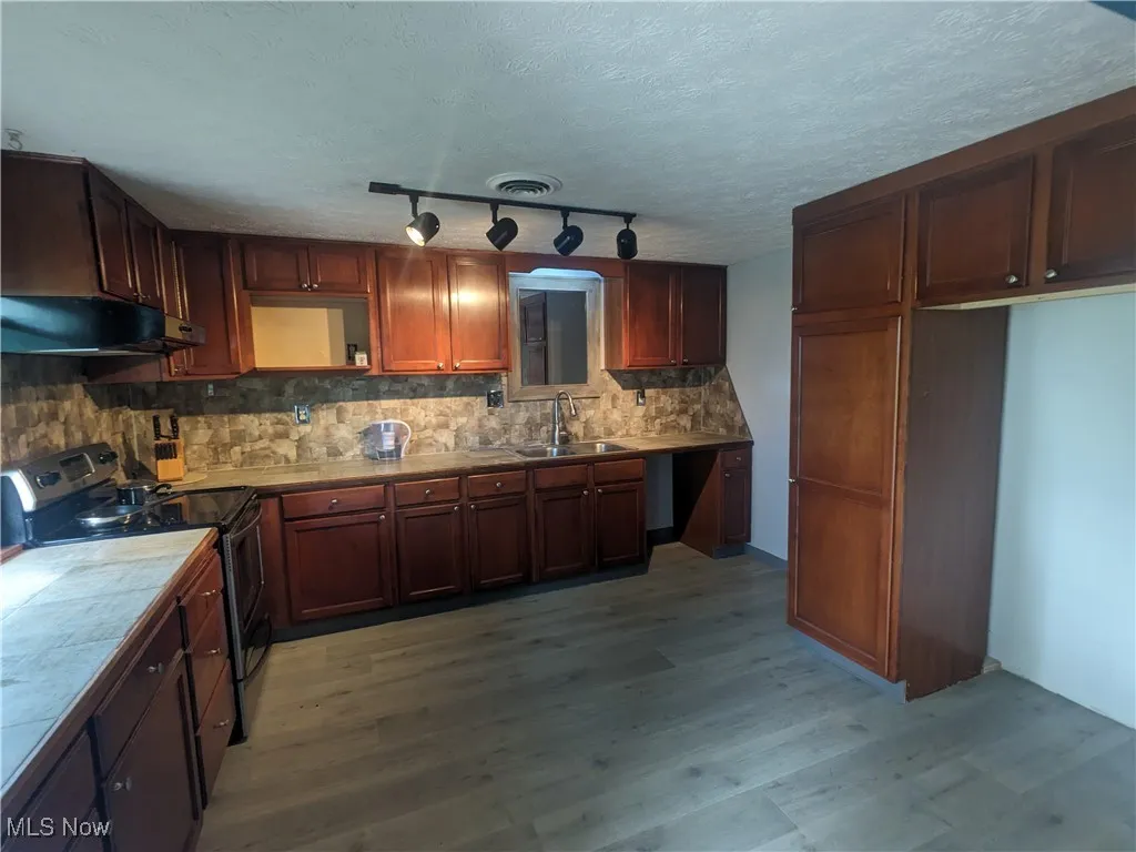 Kitchen featuring electric range oven, tasteful backsplash, under cabinet range hood, a textured ceiling, and vinyl plank flooring