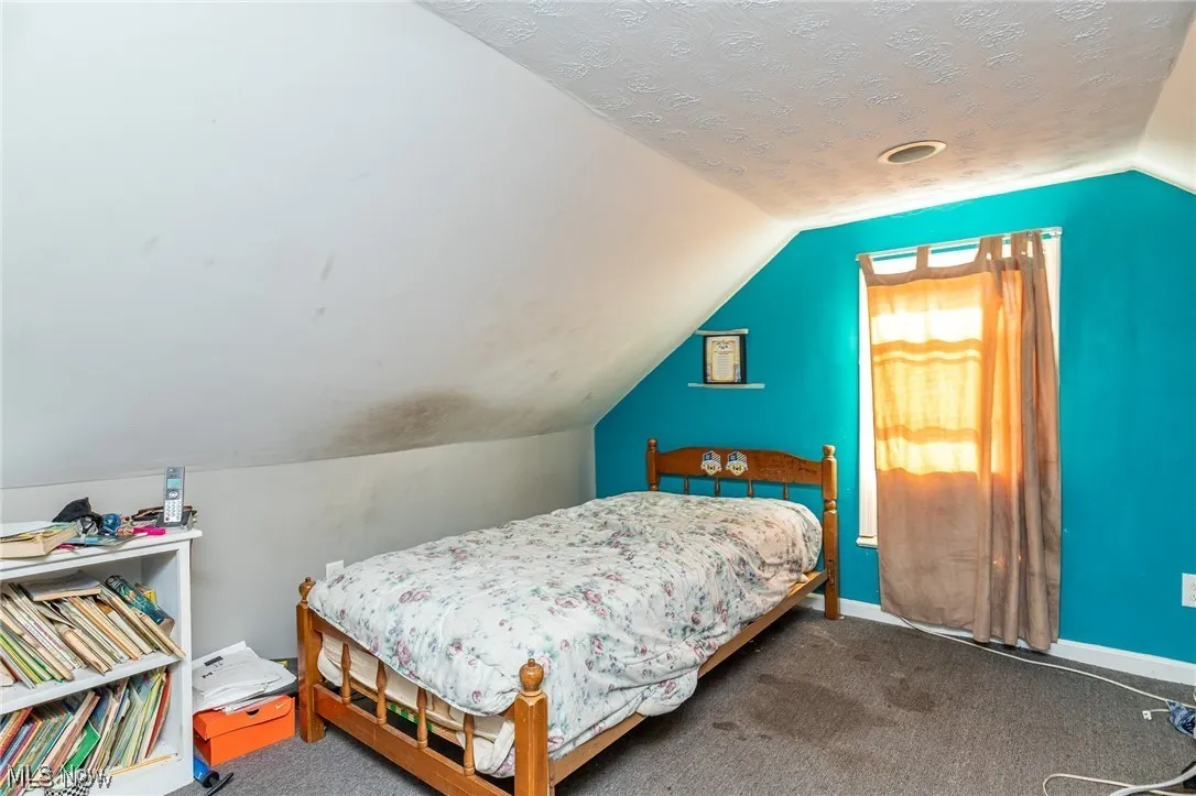 Bedroom with vaulted ceiling, carpet floors, and a textured ceiling