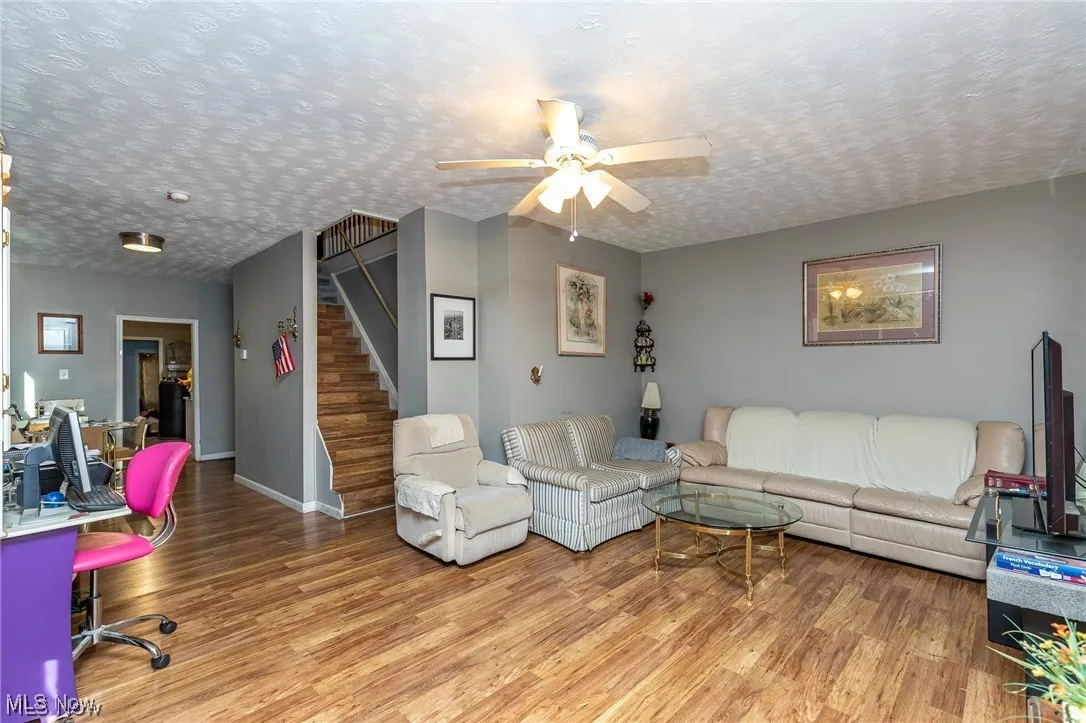 Living room with wood finished floors, ceiling fan, a textured ceiling, and stairs
