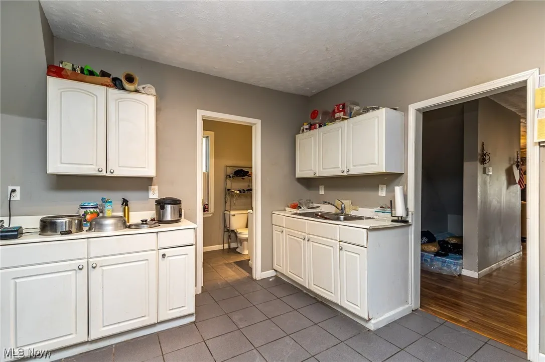 Kitchen with light countertops, a textured ceiling, white cabinetry, and dark tile patterned flooring