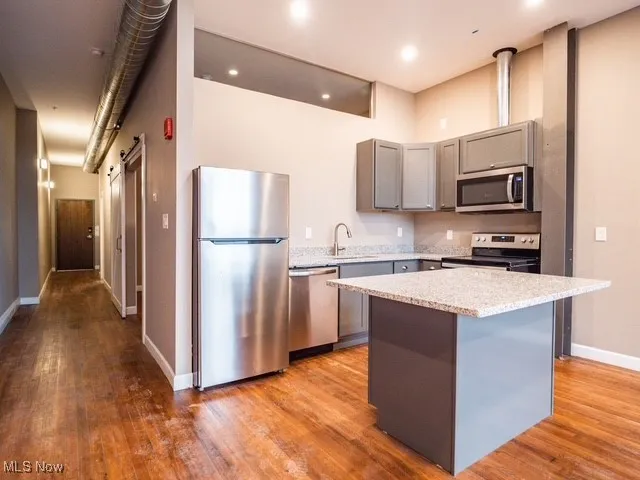 Kitchen featuring gray cabinetry, stainless steel appliances, light wood-style flooring, a center island, and light stone counters
