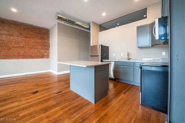 Kitchen featuring brick wall, a center island, gray cabinets, dark wood finished floors, and stainless steel appliances