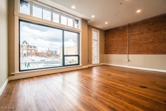 Unfurnished room with hardwood / wood-style flooring, recessed lighting, and brick wall