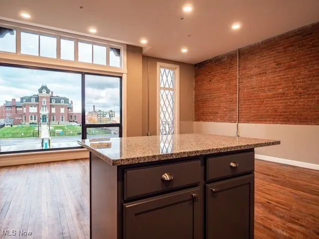 Kitchen featuring brick wall, light stone countertops, recessed lighting, a kitchen island, and wood finished floors