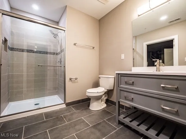 Full bath featuring vanity, dark tile patterned floors, and a stall shower