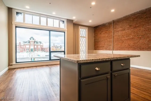Kitchen featuring brick wall, light stone countertops, a center island, light wood-type flooring, and recessed lighting