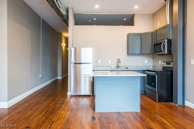 Kitchen featuring appliances with stainless steel finishes, a center island, gray cabinetry, dark wood finished floors, and light stone countertops