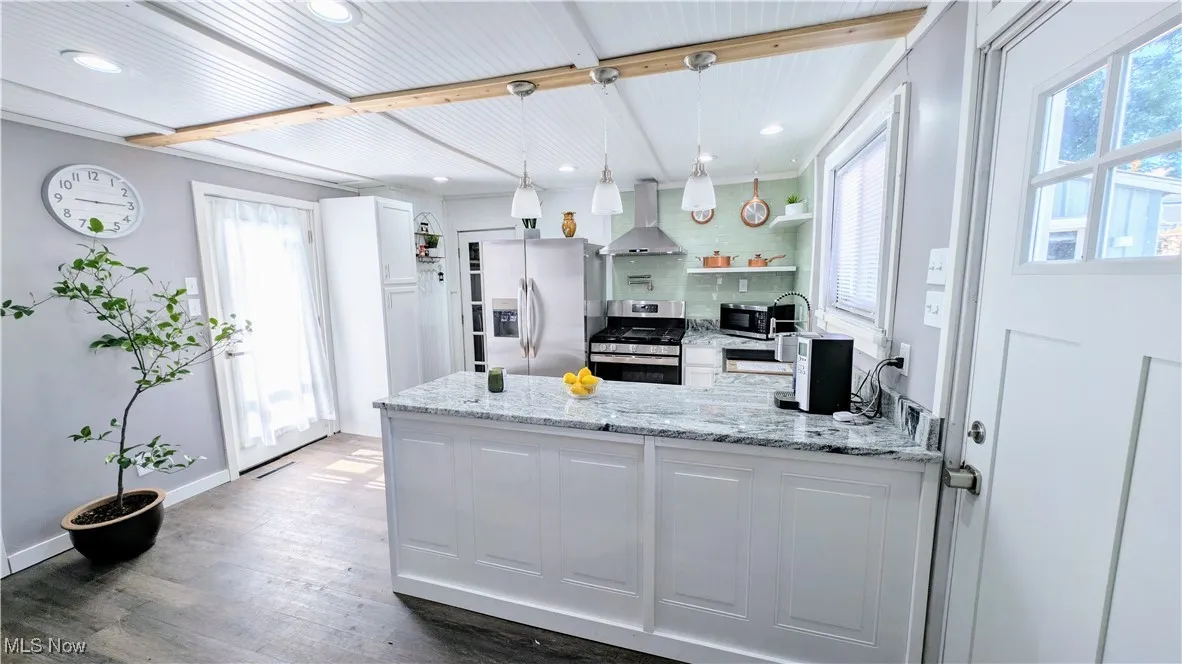 Kitchen with granite countertops, decorative light fixtures, a peninsula, appliances with stainless steel finishes, pot filler