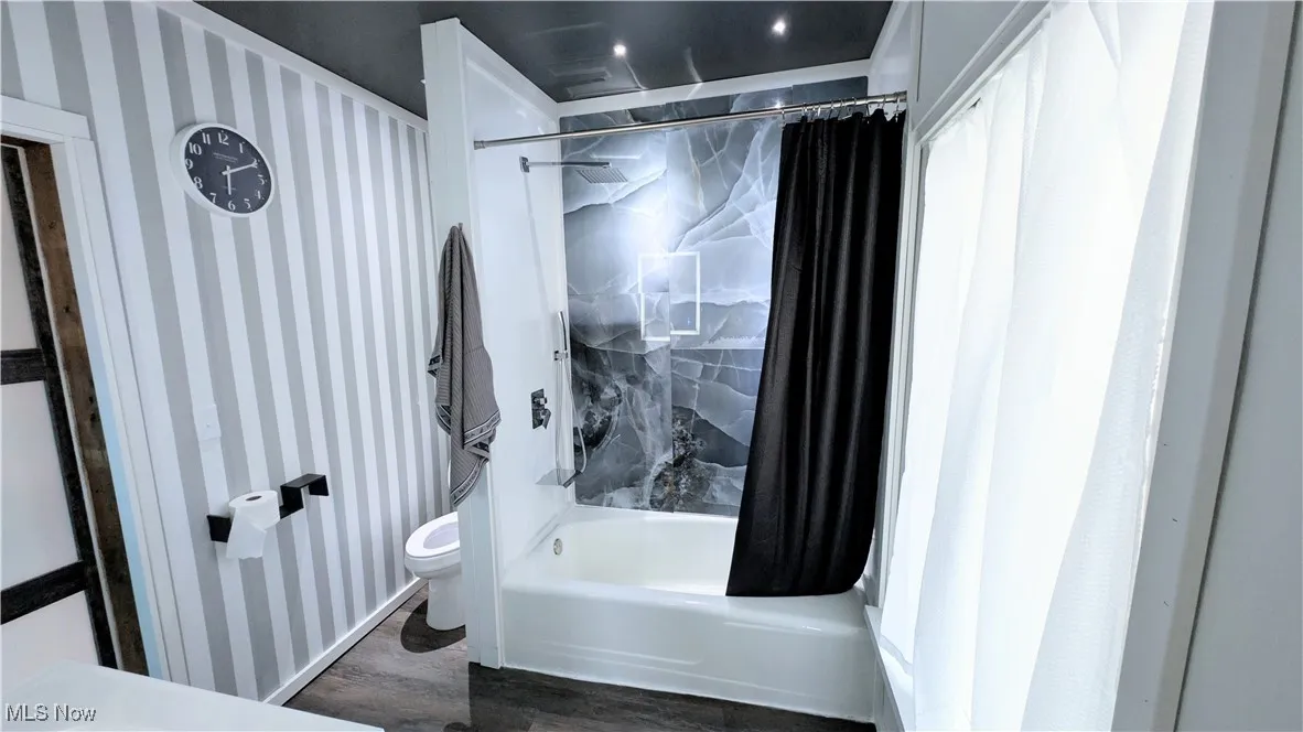 Full bath featuring shower / bathtub combination with curtain and dark wood-style floors