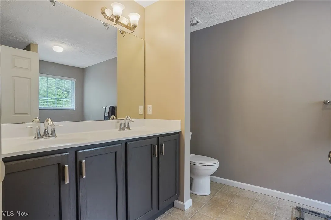 Full bathroom featuring a textured ceiling, double vanity, and light tile patterned floors
