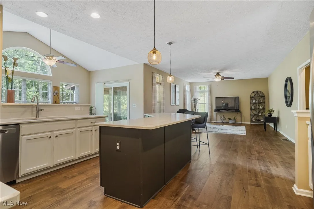 Kitchen featuring ceiling fan, open floor plan, a kitchen bar, white cabinets, and hanging light fixtures