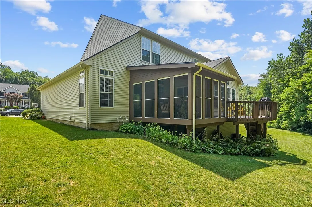 Rear view of house with a sunroom, a lawn, and a wooden deck
