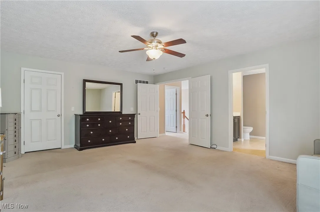 Unfurnished bedroom with light carpet, a textured ceiling, ceiling fan, and ensuite bathroom