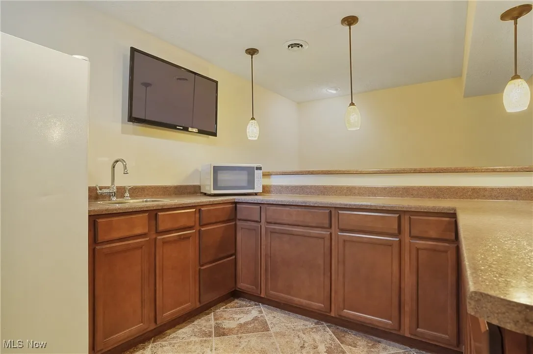 Kitchen with white microwave, pendant lighting, brown cabinets, and light countertops