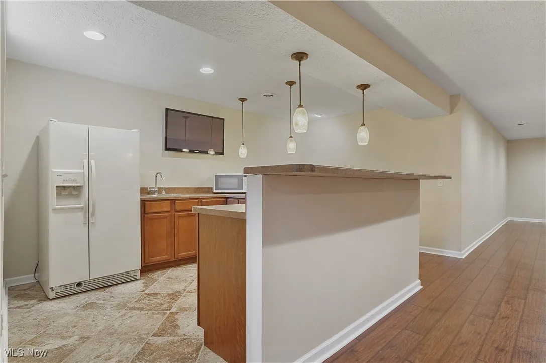 Kitchen with brown cabinets, white appliances, pendant lighting, a textured ceiling, and light countertops
