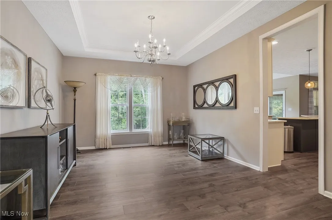 Dining space with a raised ceiling, dark wood finished floors, healthy amount of natural light, a chandelier, and crown molding