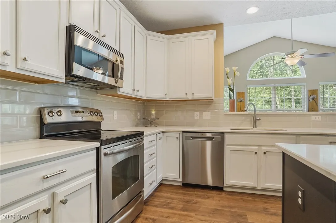 Kitchen featuring appliances with stainless steel finishes, white cabinetry, decorative backsplash, dark wood-style flooring, and lofted ceiling