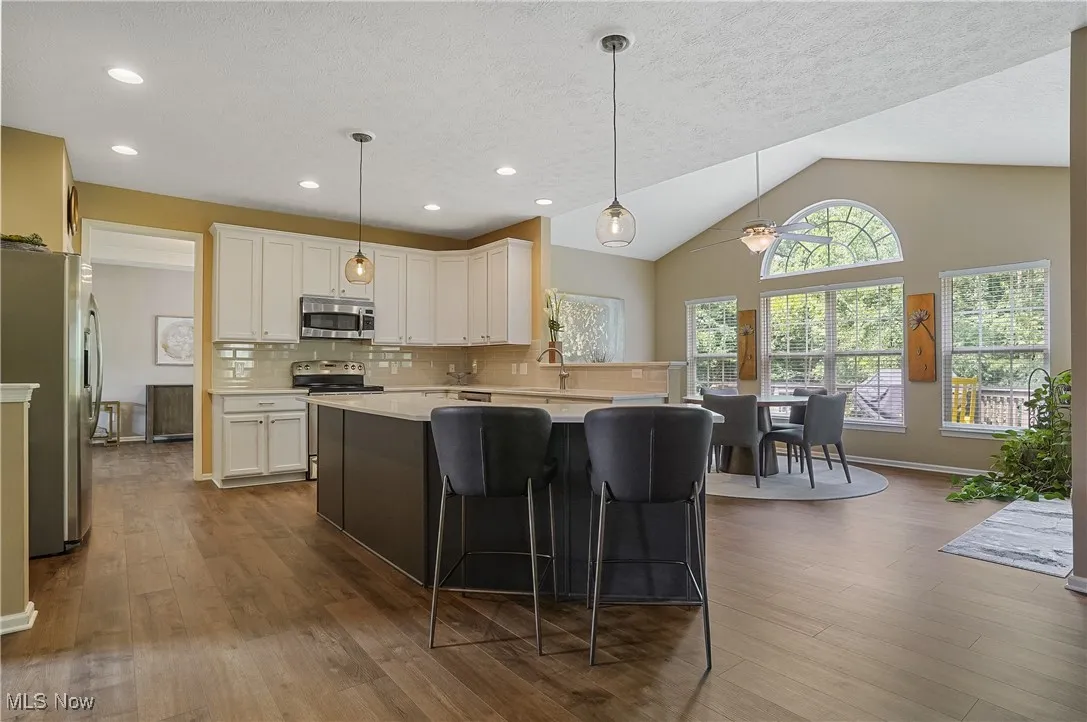 Kitchen featuring backsplash, appliances with stainless steel finishes, a kitchen breakfast bar, hanging light fixtures, and lofted ceiling
