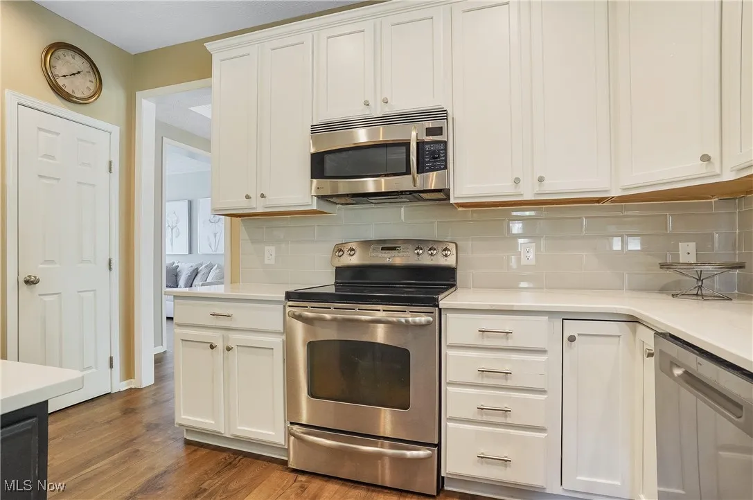 Kitchen featuring stainless steel appliances, white cabinetry, decorative backsplash, and dark wood-style flooring