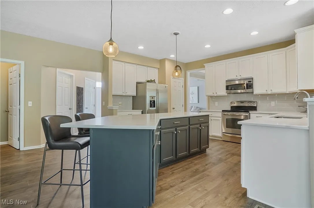 Kitchen featuring appliances with stainless steel finishes, decorative backsplash, white cabinets, hanging light fixtures, and a kitchen breakfast bar