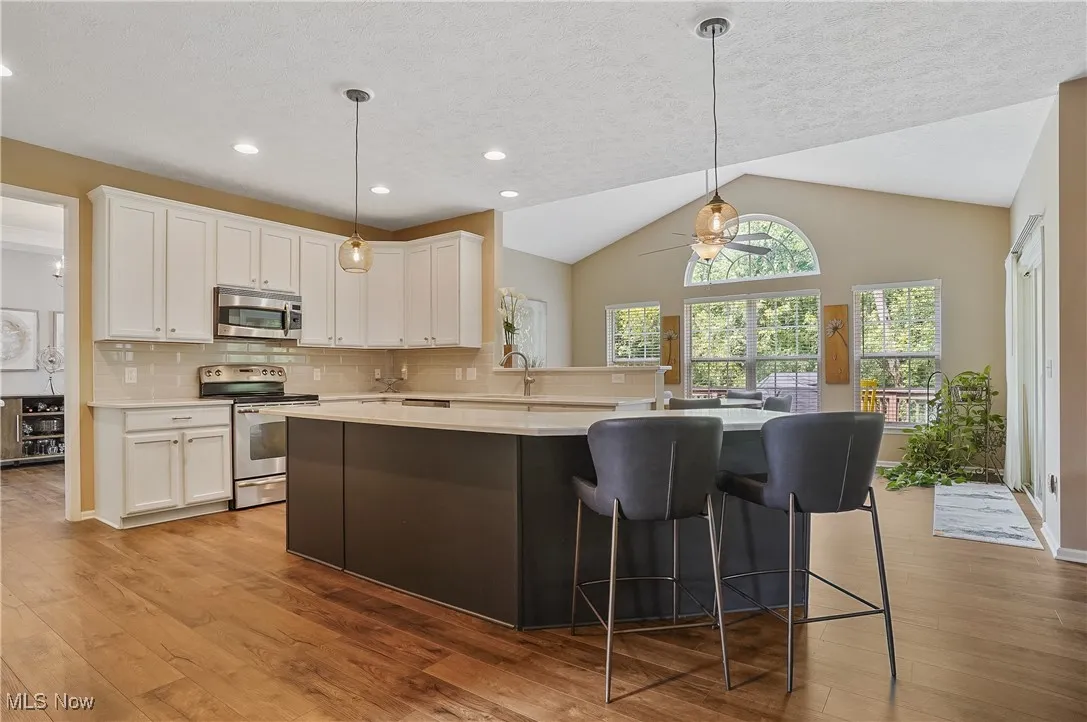 Kitchen with pendant lighting, appliances with stainless steel finishes, lofted ceiling, backsplash, and white cabinetry