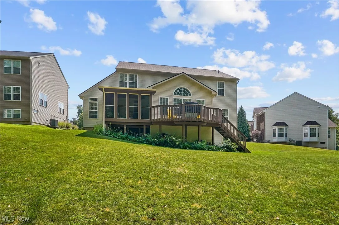 Rear view of property with a deck, a yard, a sunroom, and stairs
