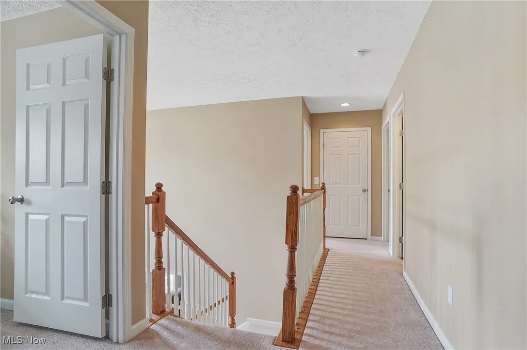 Hall with an upstairs landing, light colored carpet, and a textured ceiling