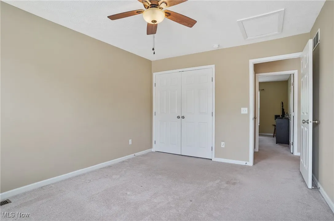 Unfurnished bedroom featuring attic access, light colored carpet, ceiling fan, and a closet