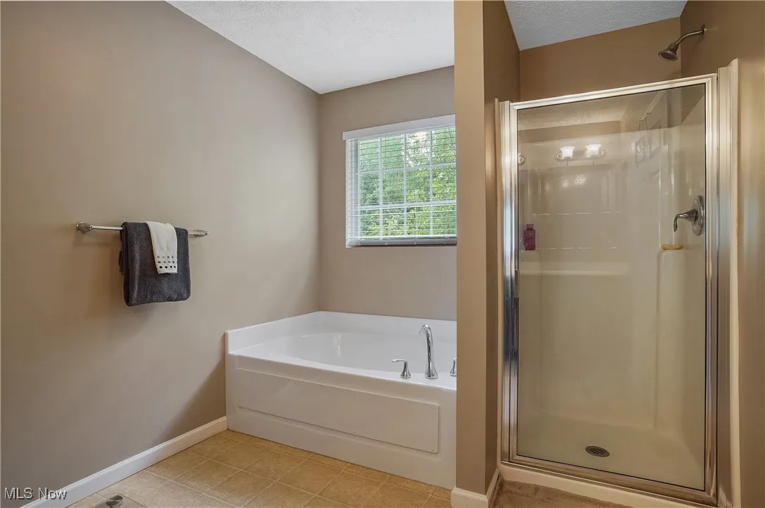 Full bath with a shower stall, a garden tub, light tile patterned flooring, and a textured ceiling