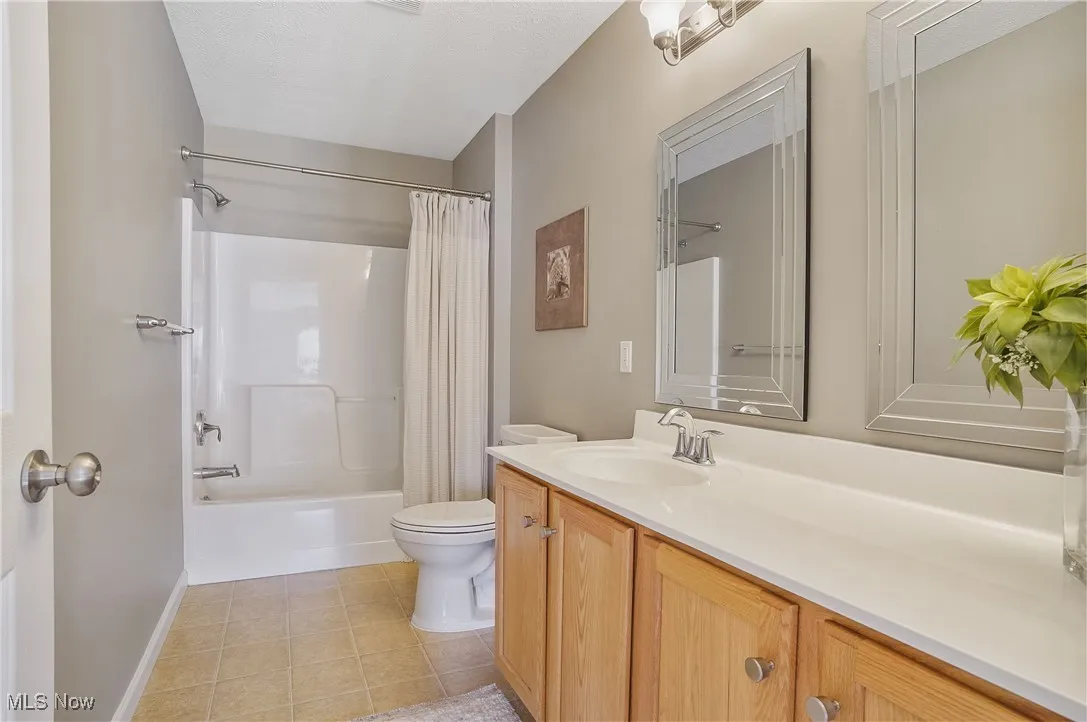 Bathroom featuring shower / tub combo with curtain, vanity, and light tile patterned floors