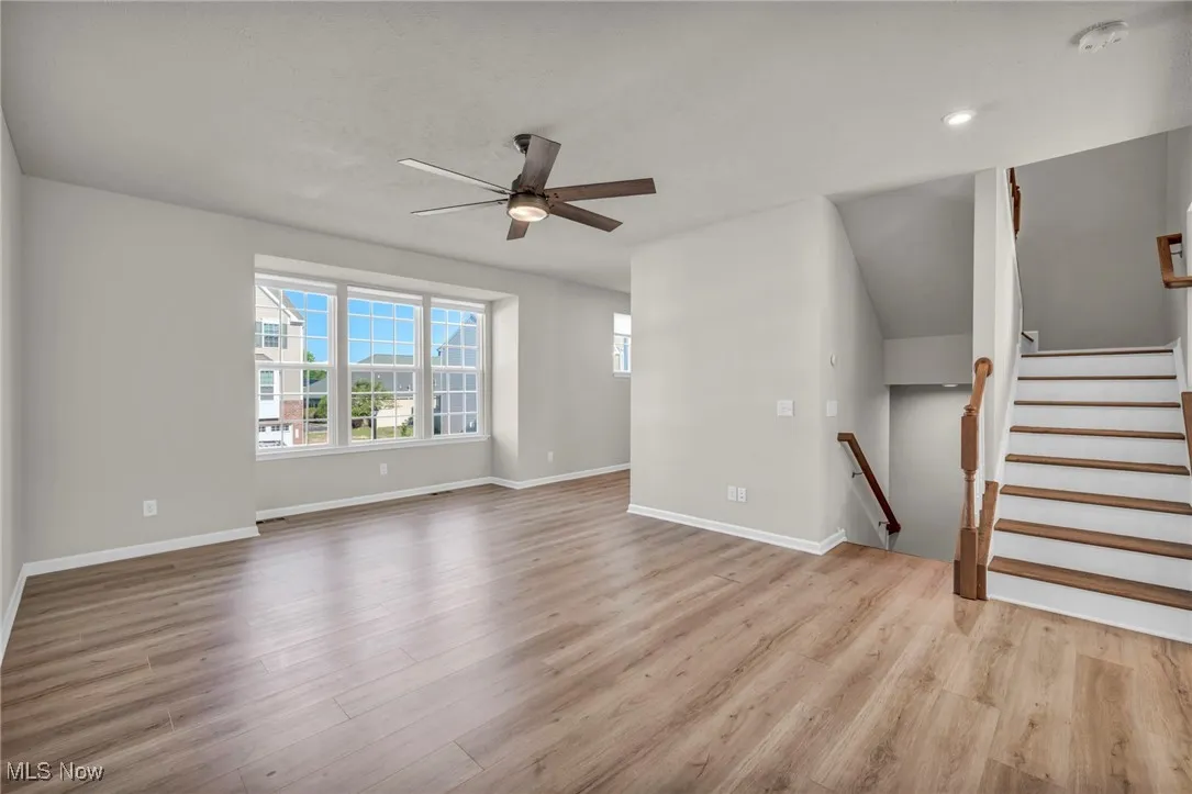 Unfurnished living room with stairway, light wood finished floors, and ceiling fan