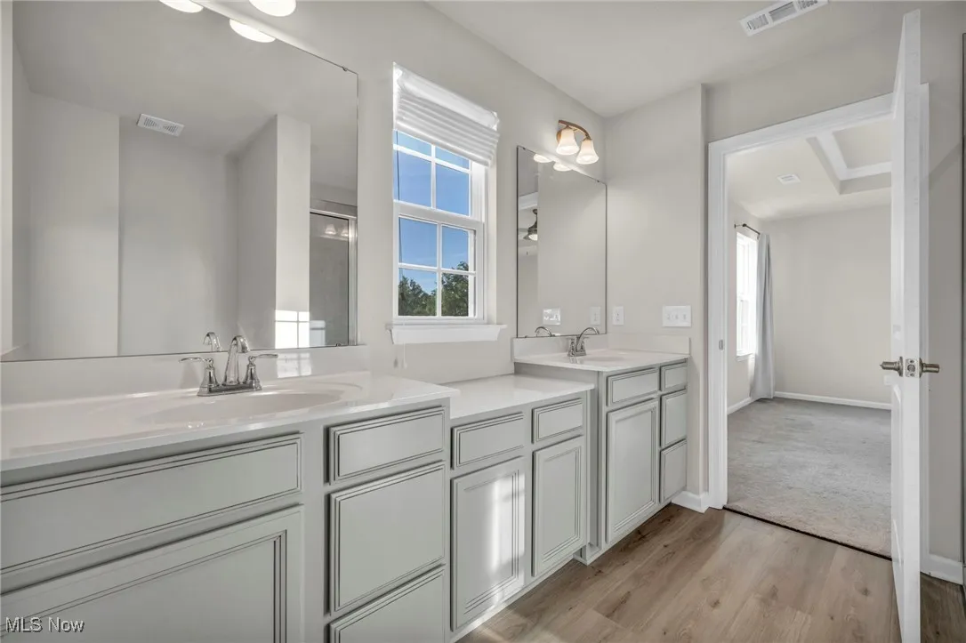 Full bath with double vanity, light wood-style flooring, and a shower with shower door
