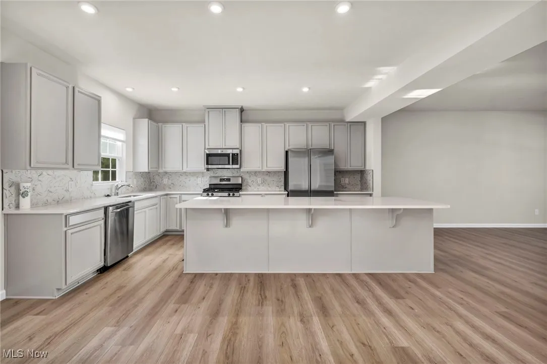 Kitchen with appliances with stainless steel finishes, light wood finished floors, tasteful backsplash, a large island, and recessed lighting