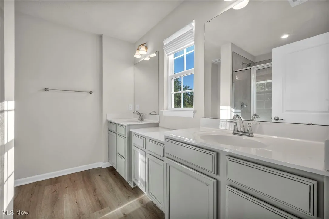 Bathroom with a shower stall, light wood finished floors, and two vanities