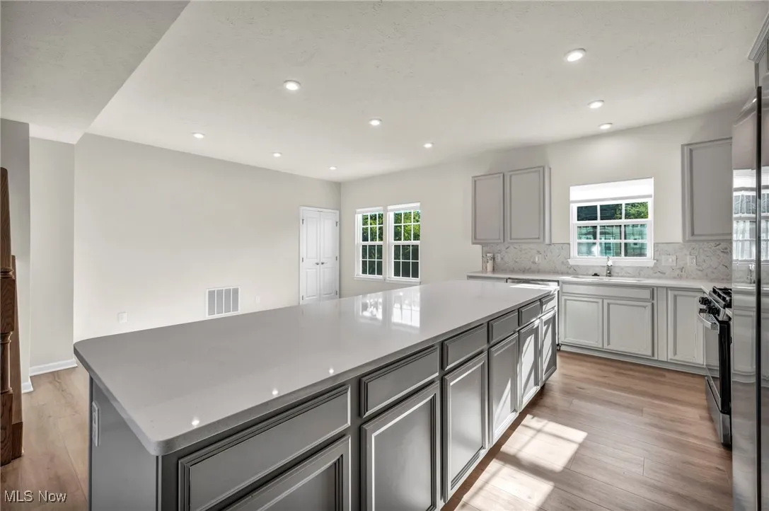 Kitchen featuring gray cabinets, light wood-style flooring, a large island, stainless steel appliances, and light stone countertops
