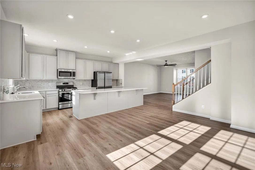 Kitchen with open floor plan, ceiling fan, tasteful backsplash, appliances with stainless steel finishes, and a breakfast bar area