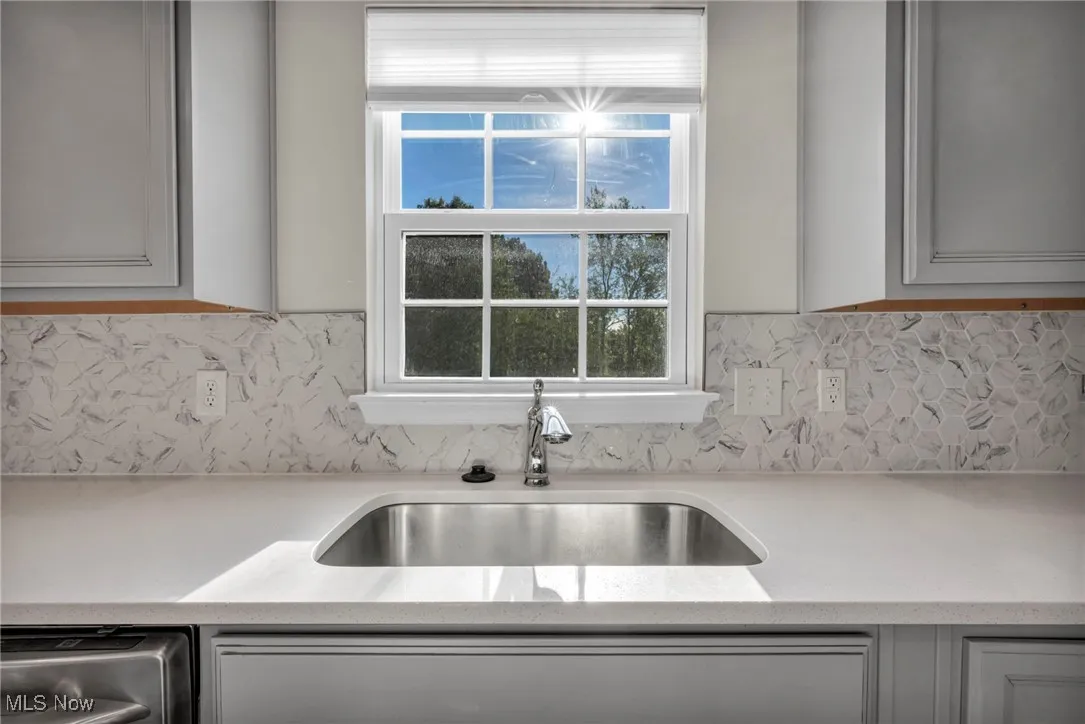 Kitchen featuring gray cabinets, light stone countertops, and decorative backsplash