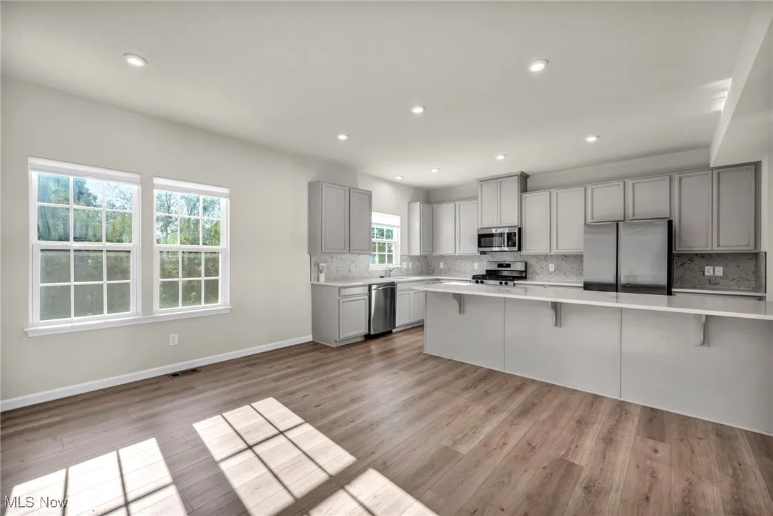 Kitchen with gray cabinetry, appliances with stainless steel finishes, a kitchen bar, tasteful backsplash, and light wood-style floors