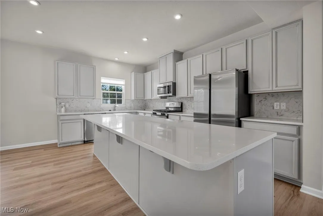 Kitchen with stainless steel appliances, a center island, light wood finished floors, recessed lighting, and a kitchen breakfast bar