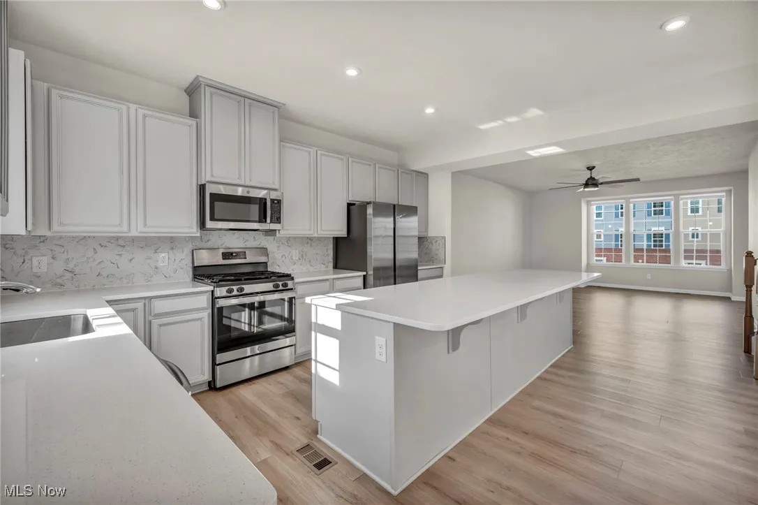 Kitchen featuring decorative backsplash, stainless steel appliances, a kitchen island, ceiling fan, and open floor plan