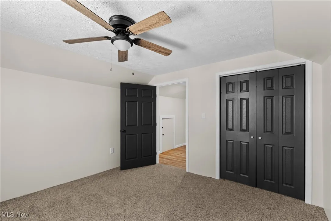Unfurnished bedroom featuring vaulted ceiling, a textured ceiling, carpet flooring, a closet, and ceiling fan