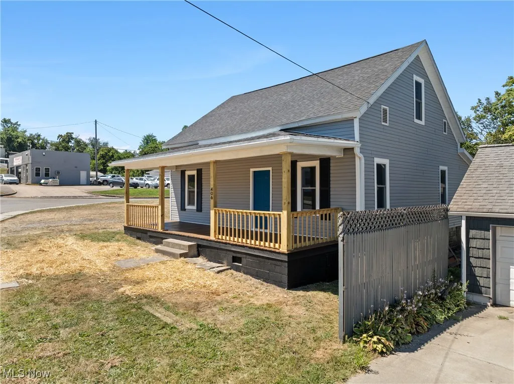 View of front facade with a porch, roof with shingles, a front yard, and an outbuilding