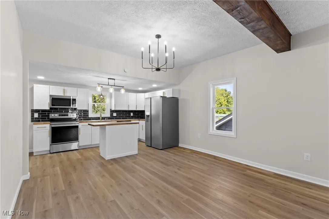 Kitchen with stainless steel appliances, a textured ceiling, white cabinets, hanging light fixtures, and a center island