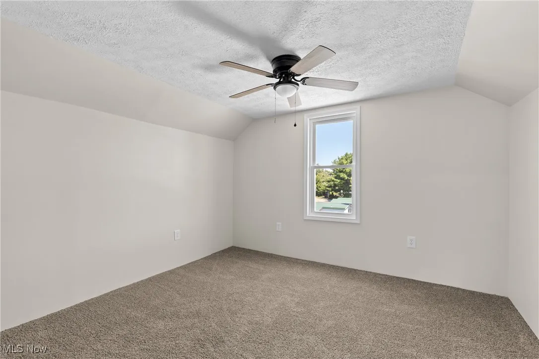 Bonus room featuring lofted ceiling, a textured ceiling, carpet, and ceiling fan